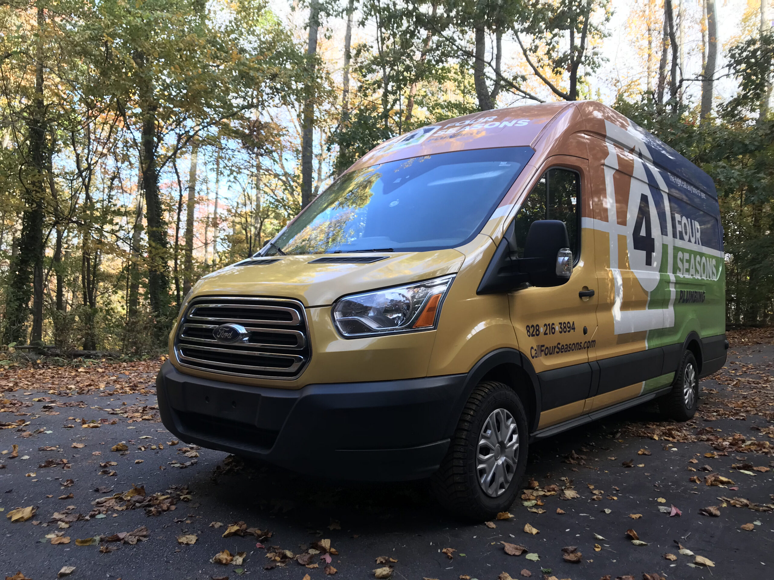 A Four Seasons service van is parked on a leaf-covered road beside trees with autumn foliage.