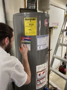 A technician writes on a service sticker attached to a Rheem water heater.